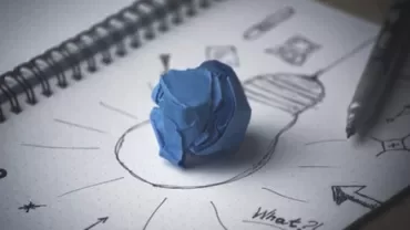 Sketch of light bulb with crumpled blue paper on notepad.