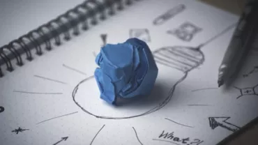 Sketch of light bulb with crumpled blue paper on notepad.