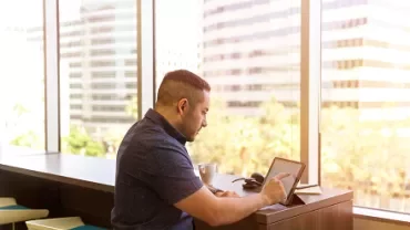 Man working on a tablet by a window with city view.