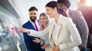 Group of business professionals collaborating with sticky notes on a glass board.