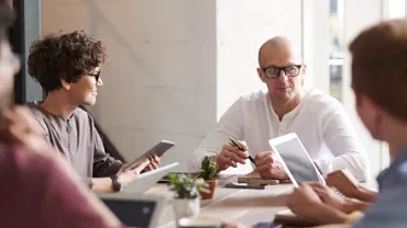 Group of people having a meeting around a table with laptops and tablets.