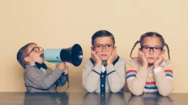 Child with megaphone shouts at bored siblings in glasses.