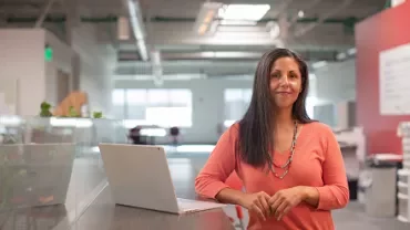 Woman in orange sweater standing by a laptop in a modern office.