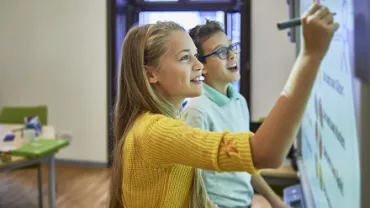 Two students using a smartboard in a classroom, engaging in an interactive lesson.
