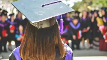 Graduate in cap and gown facing a group of fellow graduates.