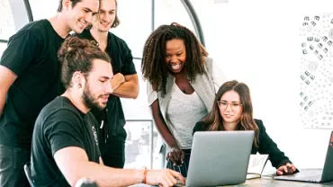 Group of people collaborating around a laptop in a bright office.