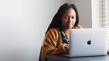 Person in a brown sweater using a laptop at a desk.