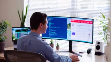 Person working at a desk with two computer screens displaying code and a website.