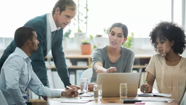 Group of people discussing around a laptop in an office.
