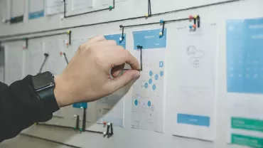 Hand arranging papers with diagrams on board using colored pins.