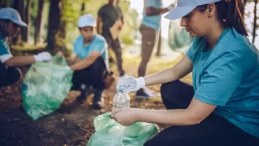 Volunteers in blue shirts and caps picking up litter in a forested area.