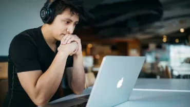 Person wearing headphones, focused on a laptop in a modern cafe.