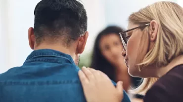 Woman comforting a man, placing her hand on his shoulder.