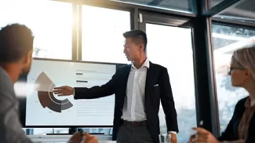 Person giving a presentation with charts on a screen in a meeting room.