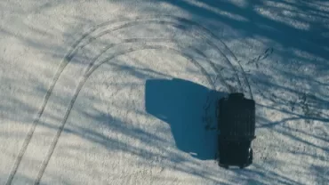 Aerial view of a black vehicle making tire tracks in the snow.