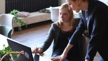 Two women working together on a laptop in an office.