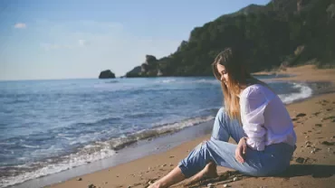Woman sitting on a sunny beach, gazing at the ocean.