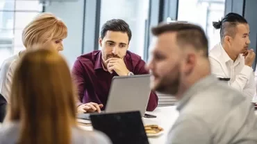 A group of people having a meeting around a table with laptops.