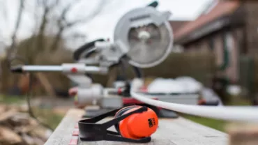 Orange ear protection and a saw on a workbench in a backyard setting.