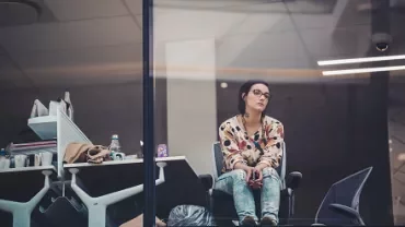 Woman in a patterned shirt sitting by a window in an office.
