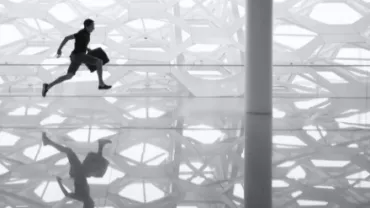 Silhouette of man running with a briefcase against geometric wall, reflected on shiny floor.