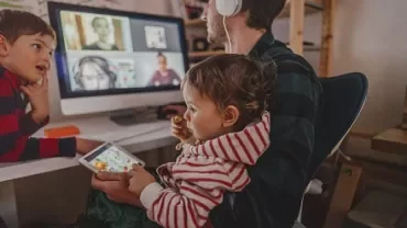 Parent working from home with children nearby during a video call.