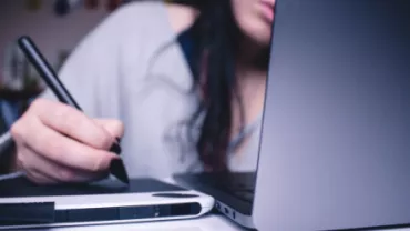 Person using a stylus on a tablet next to an open laptop.