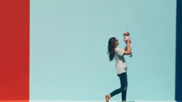 Woman holding baby against a red and blue wall.