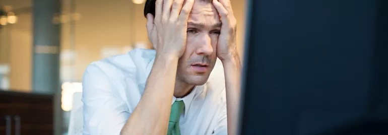 Man in office holding head in frustration