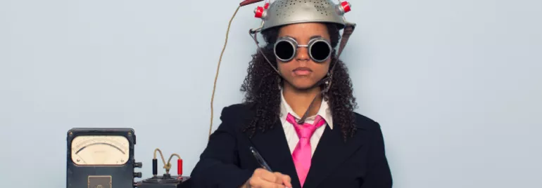 Person wearing a suit, pink tie, and goggles, with a strainer helmet connected to a device, writing in a notebook.