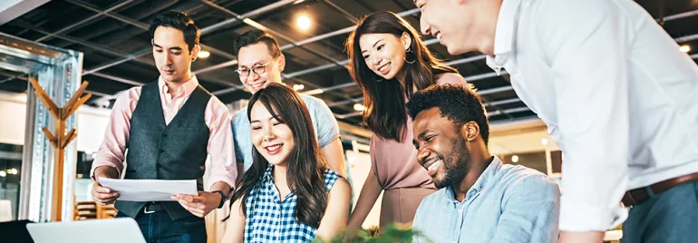 A group of colleagues collaborating at a desk, smiling and looking at a laptop.