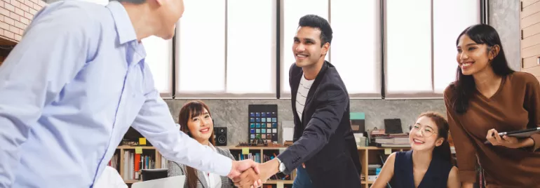 Colleagues in an office meeting, shaking hands and smiling.