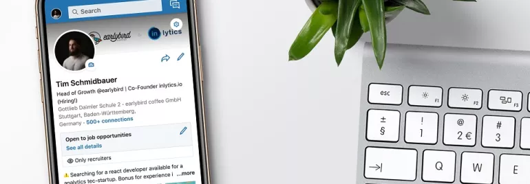 Smartphone showing a LinkedIn profile next to a keyboard and plant.