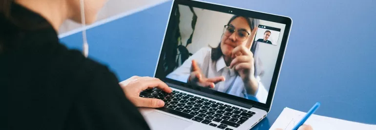 Person on laptop video call taking notes with a pen.