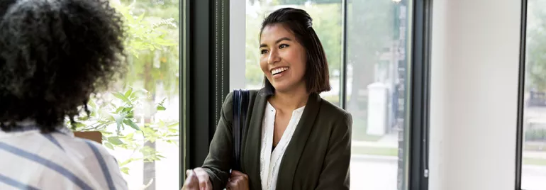 Smiling woman in business attire shaking hands near a window.