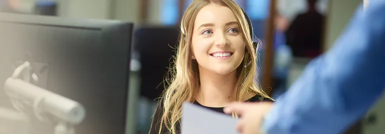 Smiling woman at her desk in an office setting, receiving a document.