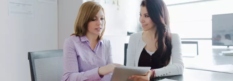 Two women in an office discussing something on a tablet.