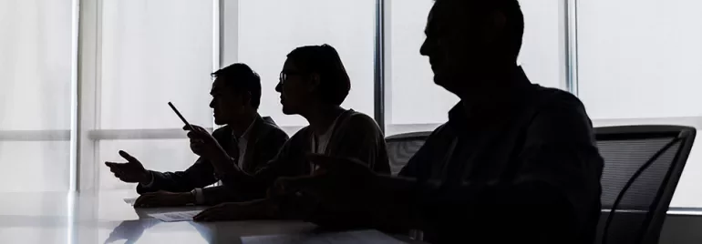 Silhouettes of three people sitting at a table during a discussion.