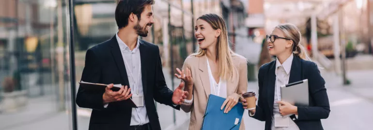 Three professionals walking and talking outside near office buildings.