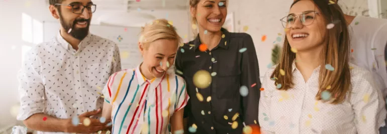 Group of people smiling and laughing with colorful confetti falling around them.