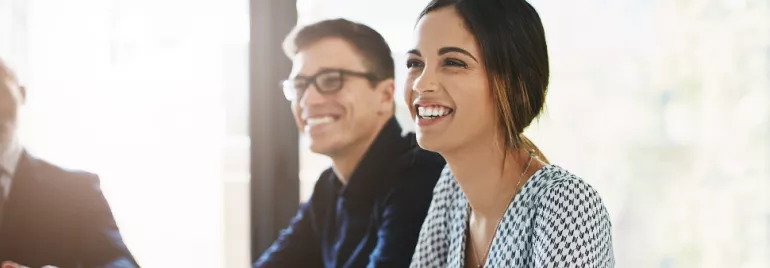 Two people smiling and sitting at a table in an office setting.