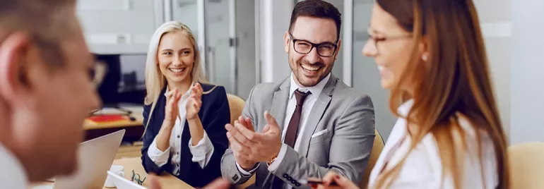 Group of professionals smiling and clapping in a modern office meeting.