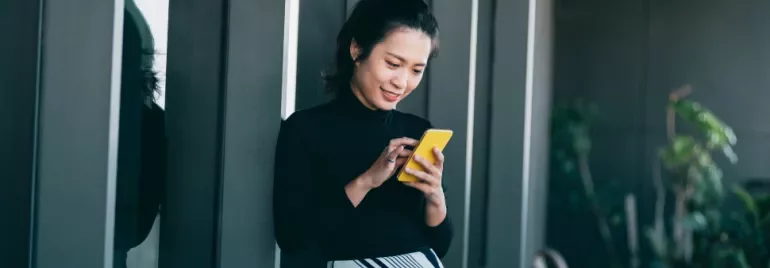 Woman smiling while using a yellow smartphone outside a building.