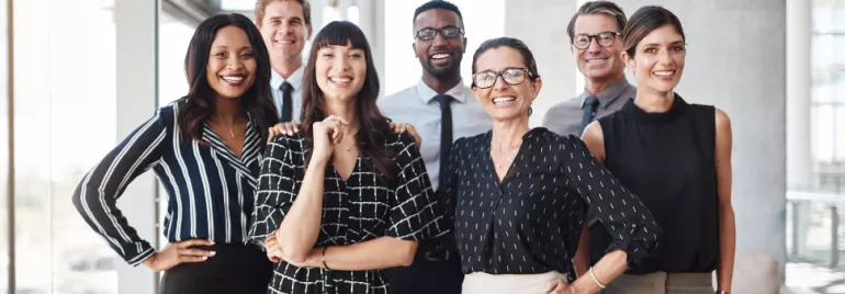 Group of eight professionals in business attire smiling in a modern office setting.
