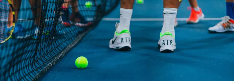 Tennis players on a blue court with tennis balls scattered around.