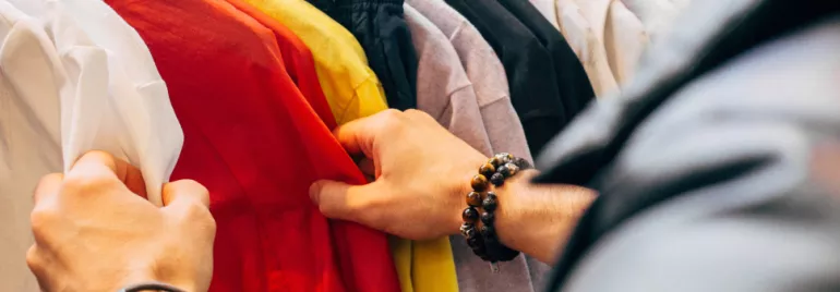 Person browsing colorful shirts on a clothing rack.