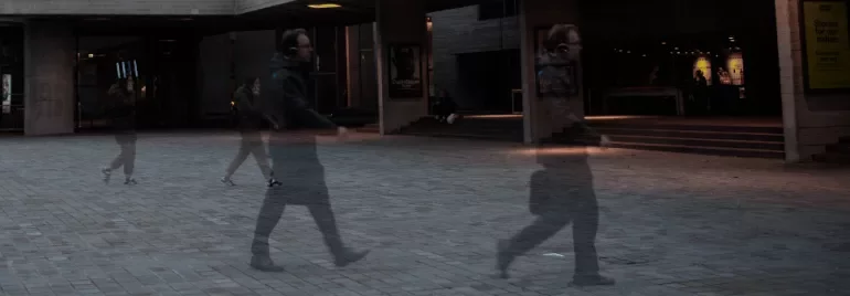 Blurred motion of people walking outside a theatre at night.