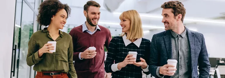 Four colleagues walking and holding coffee cups while smiling.