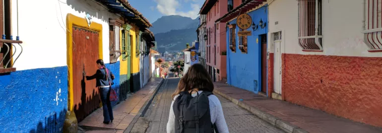 Person walking down a colorful street with mountains in the background.