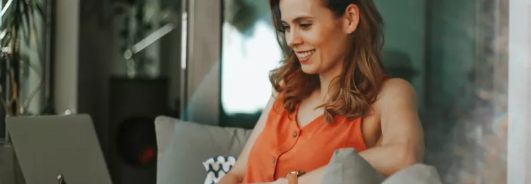 Woman smiling while using a laptop on a cozy sofa.